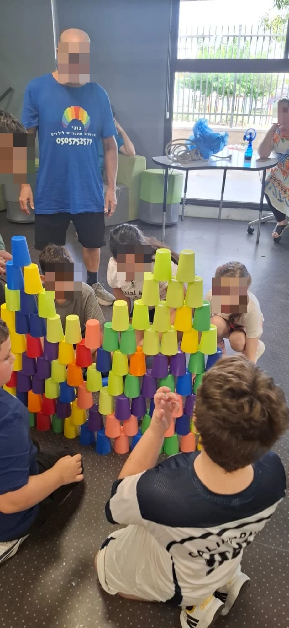 ילדים בונים מגדל כוסות צבעוני סביב שולחן בתחנת משחק רגועה של נוני